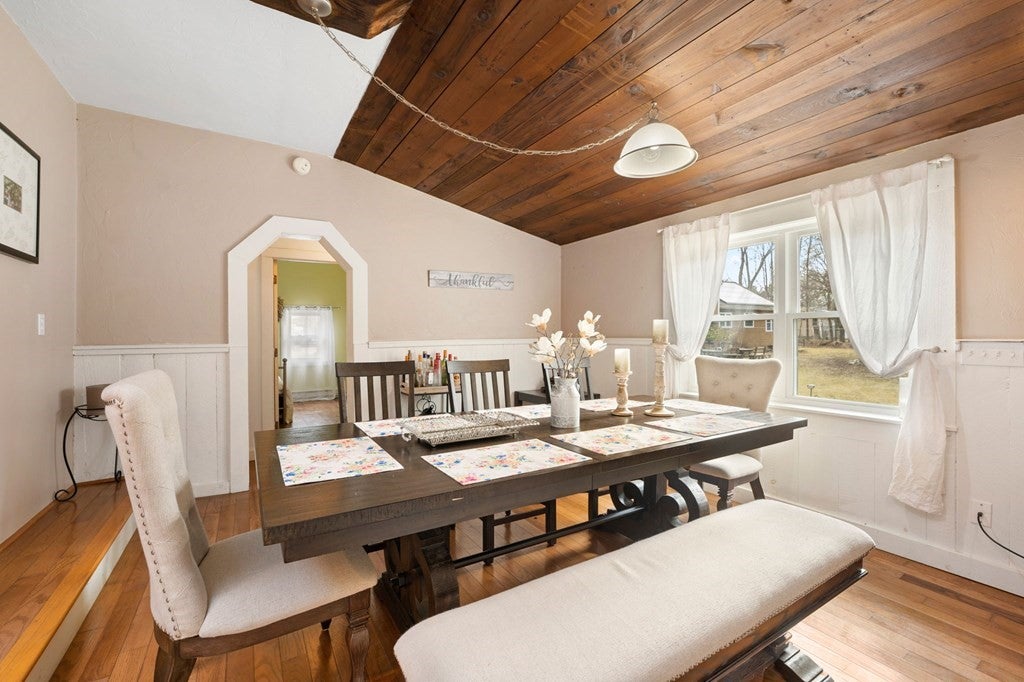 Dining room with wooden ceiling and floors.  White paneled and beige walls.  Dining table with bench and chairs.