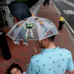 A father holds an umbrella decorated with characters from Disney's Toy Story, while his son stands to the left of him and looks at the camera.