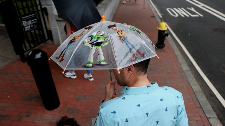 A father holds an umbrella decorated with characters from Disney's Toy Story, while his son stands to the left of him and looks at the camera.