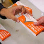 Someone hands out a white and orange COVID-19 Antigen Rapid Test kit to a Salem resident in Massachusetts in 2021.