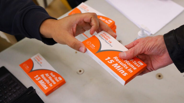 Someone hands out a white and orange COVID-19 Antigen Rapid Test kit to a Salem resident in Massachusetts in 2021.