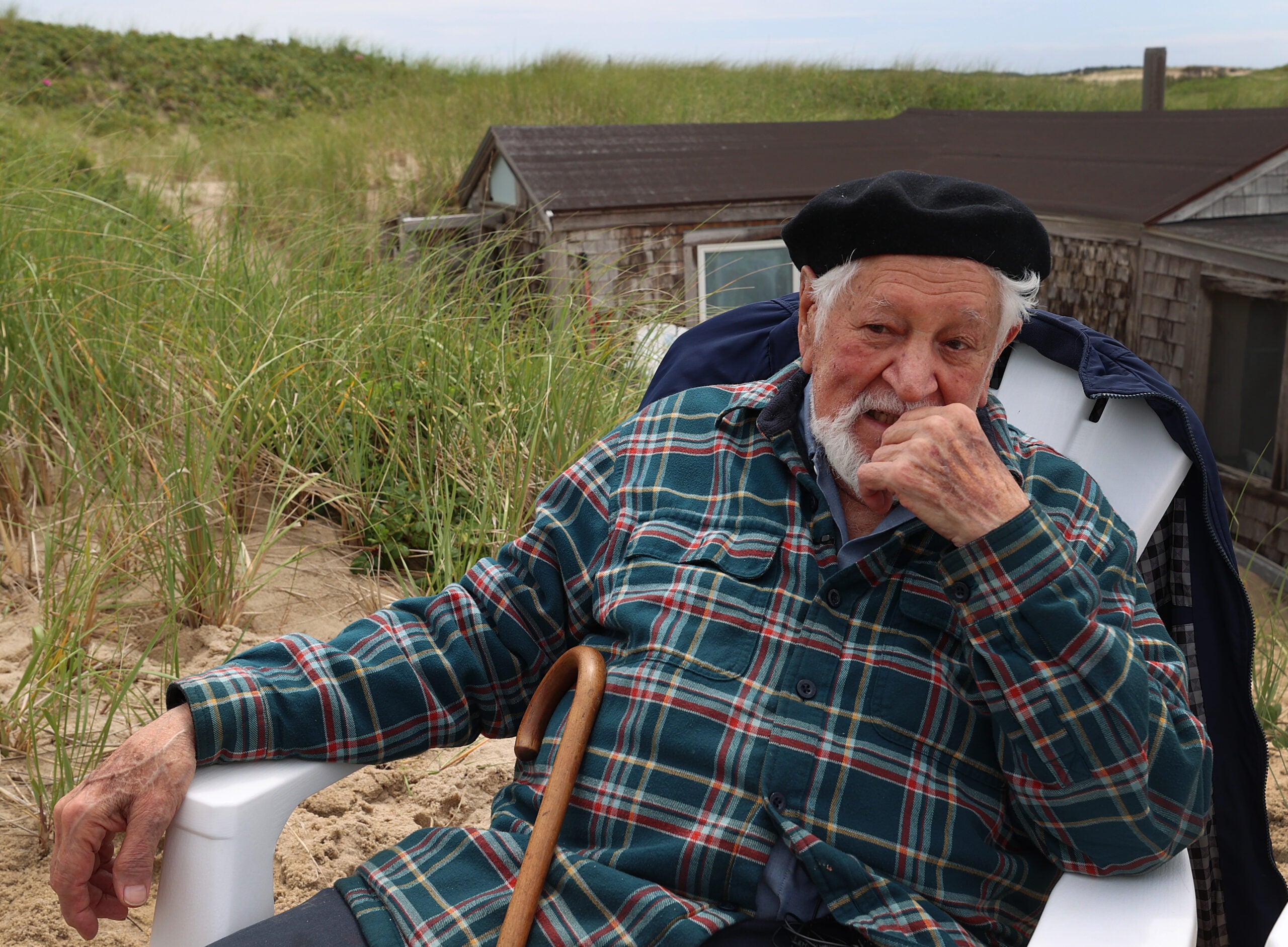 Provincetown, MA - 6/27/2023: 27DUNESHACK.....   Artist Salvatore Del Deo  sat in front of the shack,( shack in background )  Supporters gathered for a sit-in on the day of his eviction by the National Park Service at the dune shack he's occupied with his family for 77 years. The site of Frenchie's Shack, a driftwood dune shack on the National Seashore, where the NPS has ordered the eviction of the Del Deo family.(David L Ryan/Globe Staff ) SECTION:  LIVINGARTS