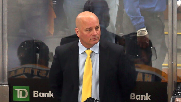Bruins coach Jim Montgomery stands at the bench as Florida players celebrate on the ice after they beat the Bruins ion overtime.