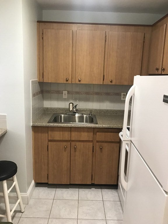 Kitchen in boston apartment with white tile floor, and wood cabinets. rent