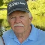 A picture of a man wearing a gray hat that says "Titleist" and a light blue polo shirt.