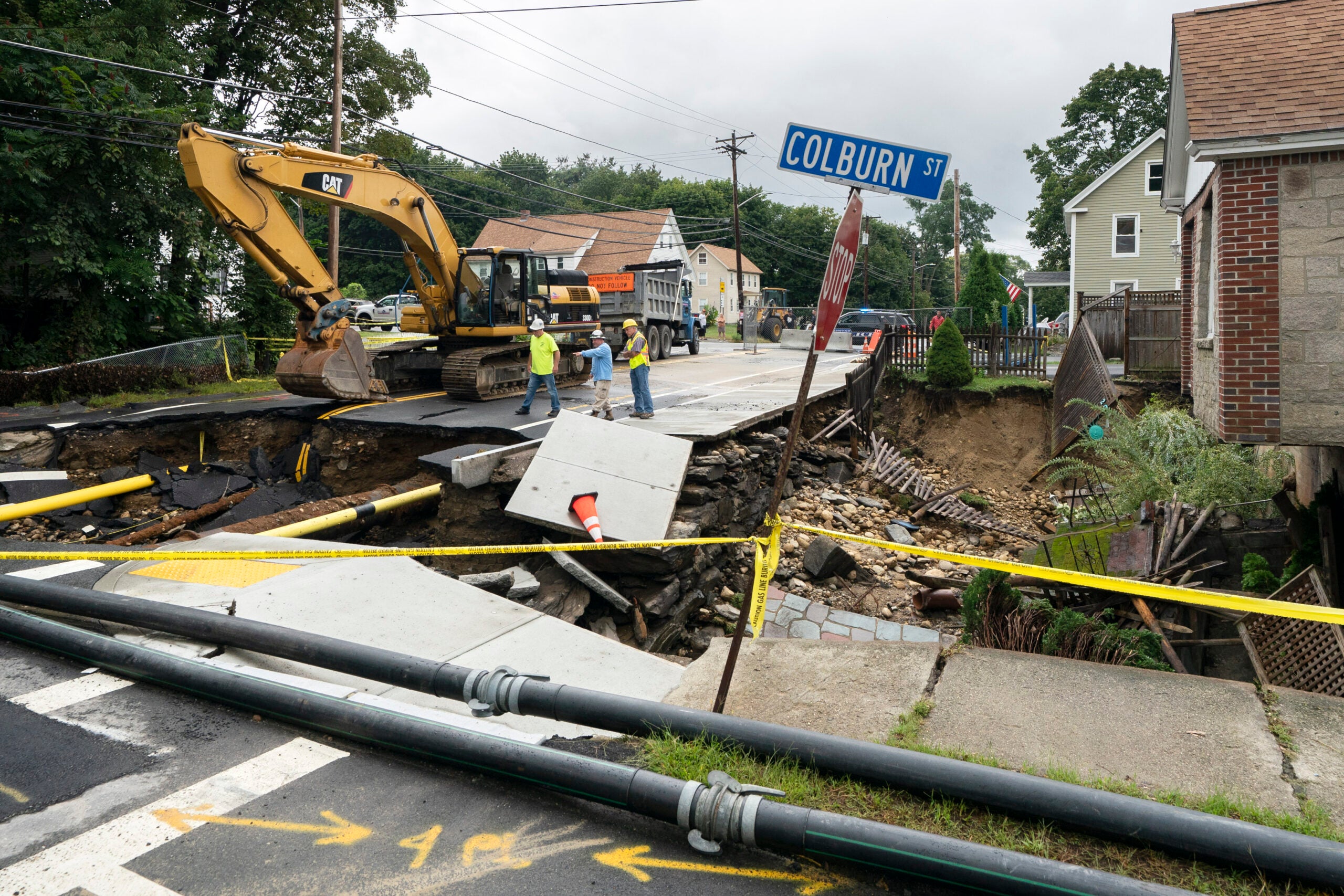 Public works officials examine the damage to a road and front yard that was washed away by recent flooding.