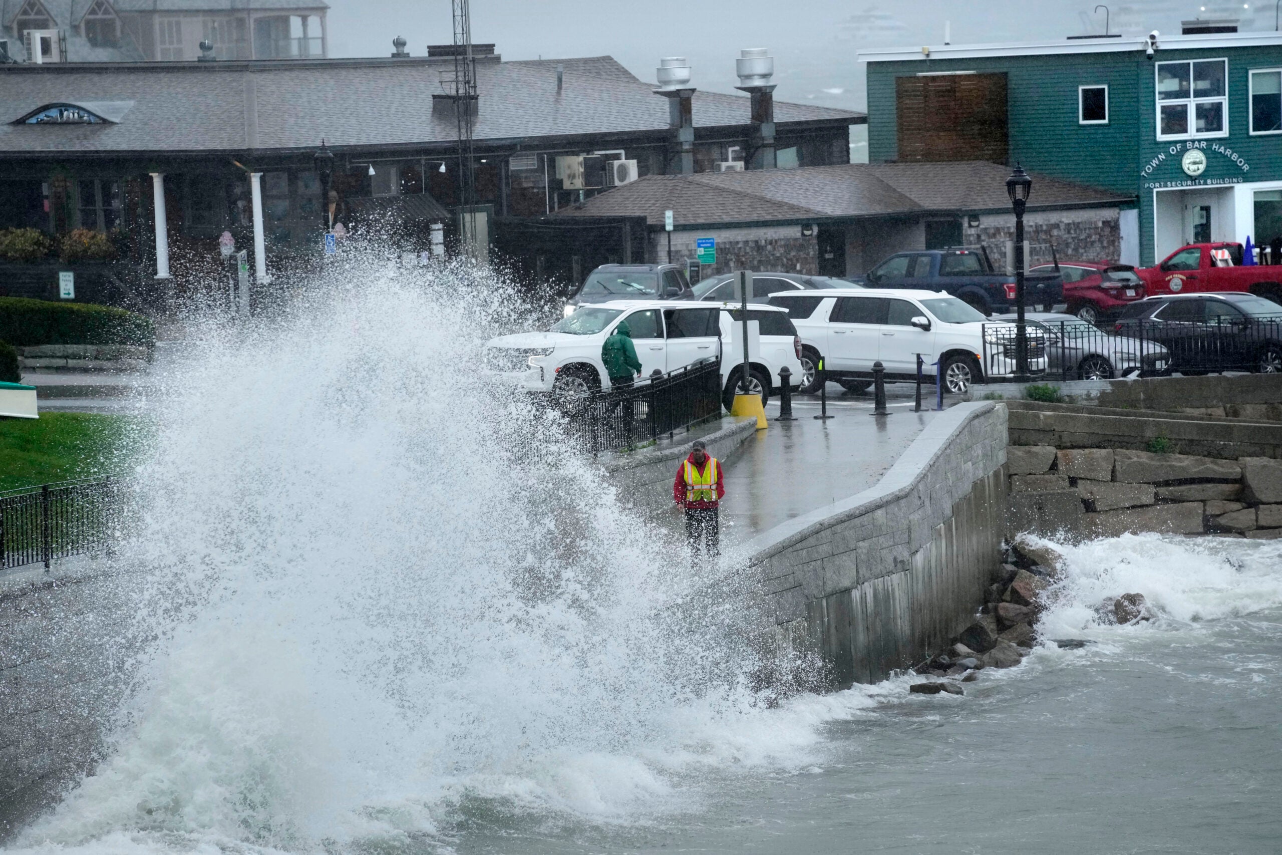 A city worker views a wave crashing along a walkway in Bar Harbor, Maine. 