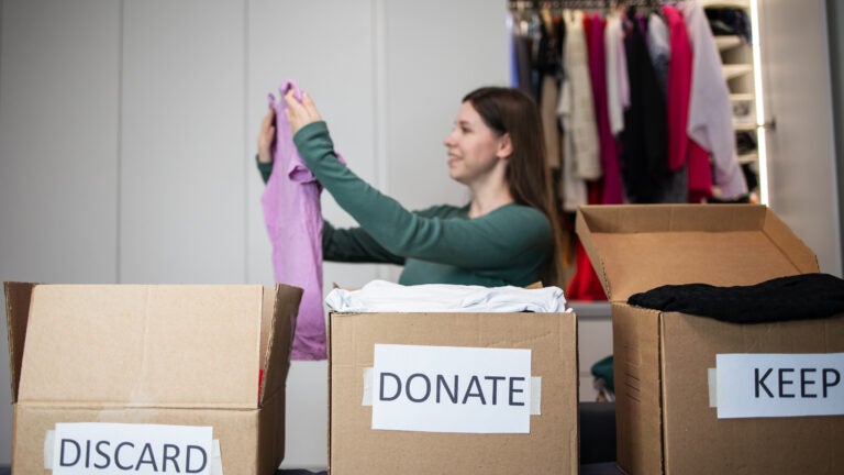 Unrecognizable woman sorts through her wardrobe. Three craft cardboard boxes of keep, discard, donation, donate. Charity clothing donations, help low income families, recycling, declutter, sustainable