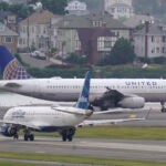 A Jet Blue flight is on the runway behind a United flight at Boston's Logan International Airport.