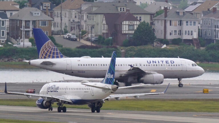 A Jet Blue flight is on the runway behind a United flight at Boston's Logan International Airport.