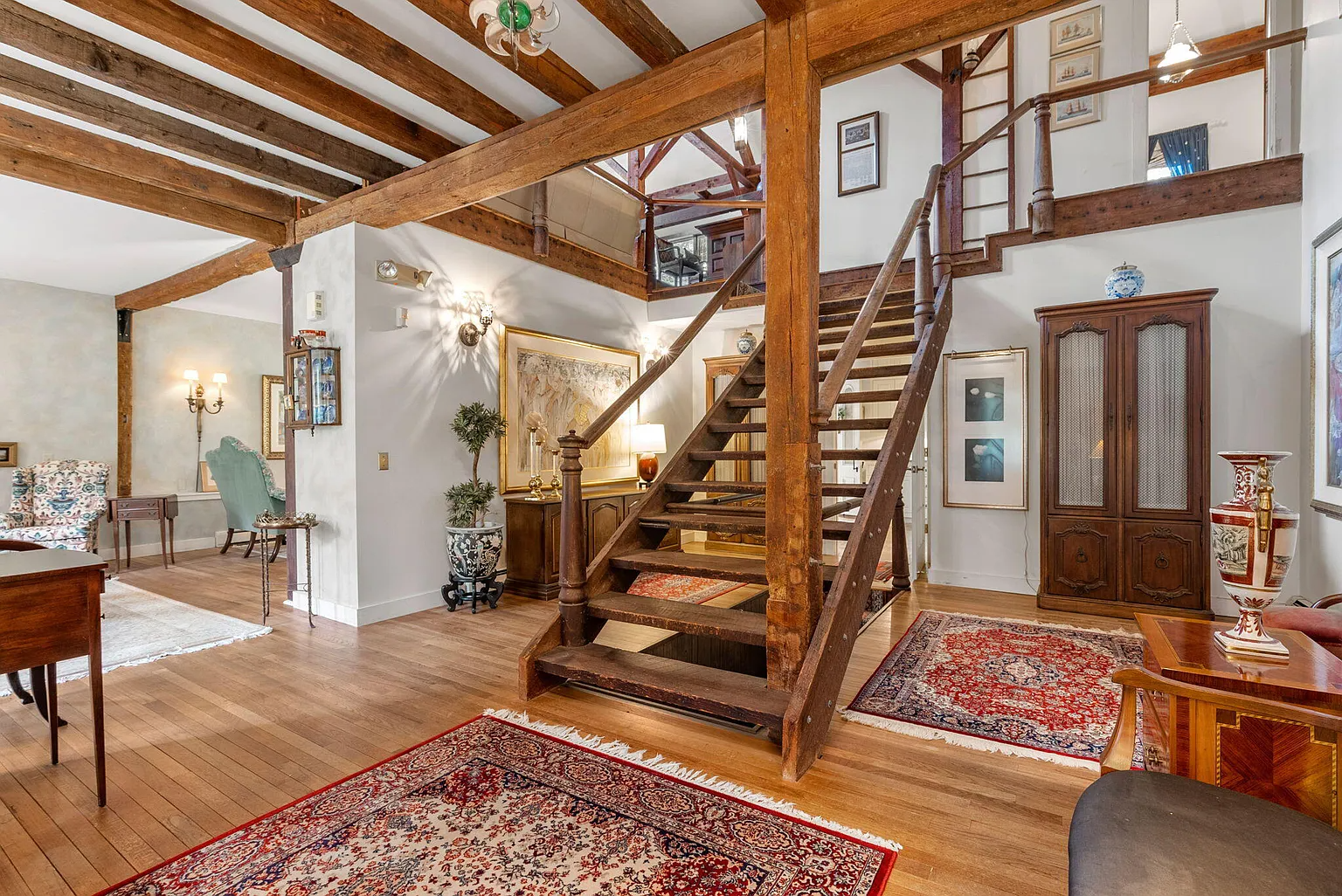 Entryway to Barnstable home with wooden beams, and grand staircase. 