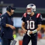 New England Patriots offensive coordinator Bill O'Brien speaks with quarterback Mac Jones (10) as quarterback Bailey Zappe (4) looks on during the second half of an NFL football game against the Philadelphia Eagles, Sunday, Sept. 10, 2023, in Foxborough, Mass.