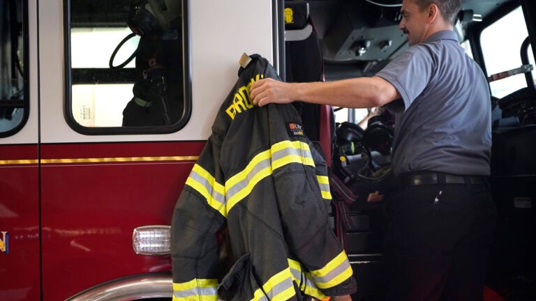 A Brockton firefighter lifts a protective turnout coat onto a firetruck.