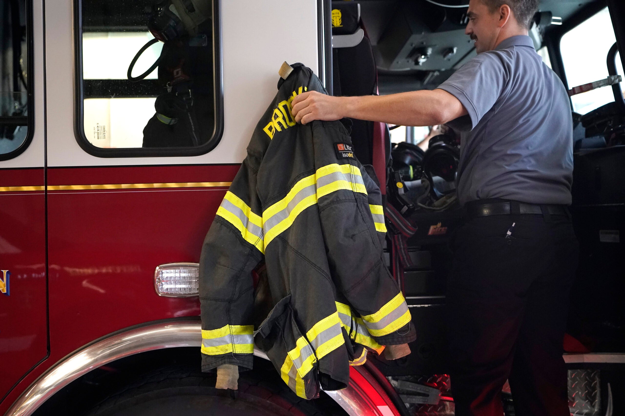 A Brockton firefighter lifts a protective turnout coat onto a firetruck.