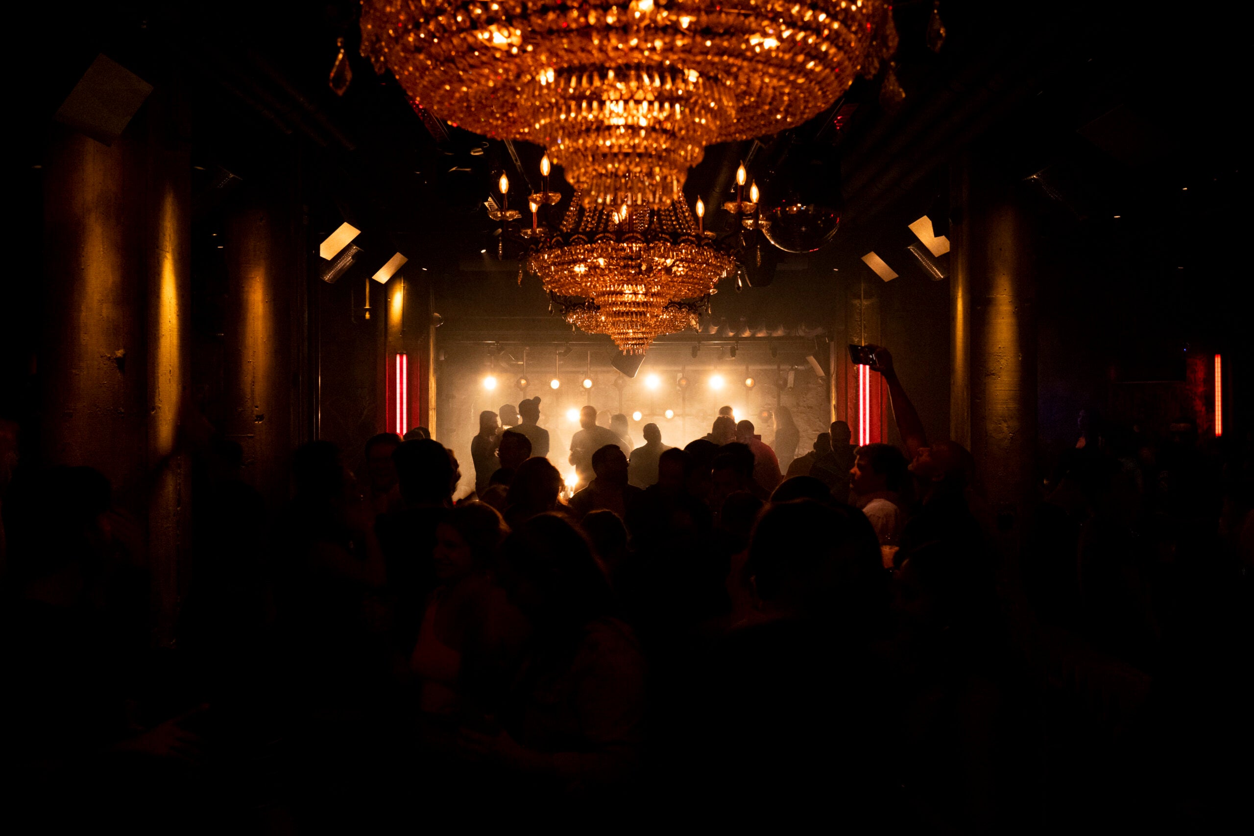 A dim nightclub in Boston, showing silhouetted patrons in front of a stage. A chandelier hangs above the crowd.