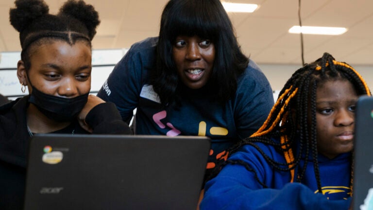 Kabila Williams, a senior technical curriculum developer at Amazon, instructs high schoolers Laniya Sanders, left, and Eboni Maxwell, right, on Alexa coding skills during a “Day of A.I.” event held in collaboration with Amazon Future Engineer and organized by the Massachusetts Institute of Technology’s “Responsible A.I. for Social Empowerment and Education” (RAISE) program, at Dearborn STEM Academy, a public school in Boston, Mass. on May 18, 2023.