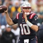 Mac Jones, in a blue New England Patriots jersey, sets up to throw a football.