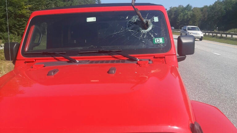 A red Jeep with a piece of metal sticking out of the windshield.