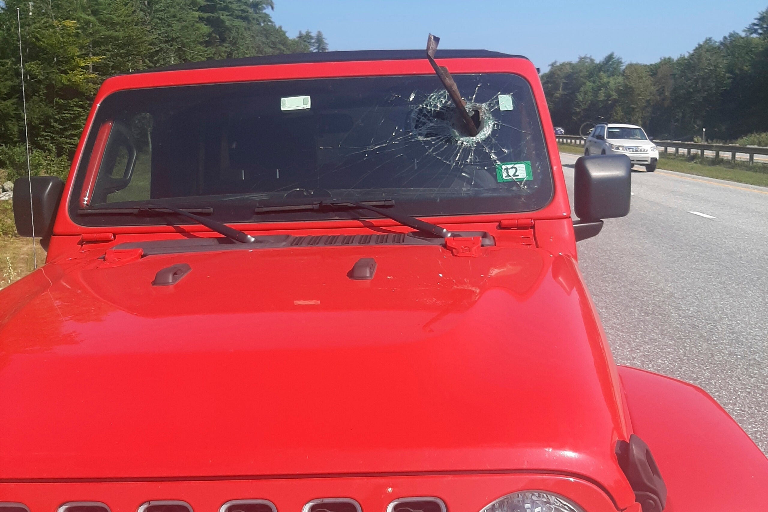 A red Jeep with a piece of metal sticking out of the windshield.