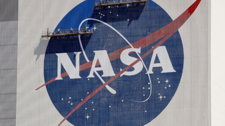 Workers on scaffolding repaint the NASA logo.