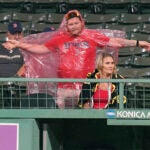 A Red Sox fan stretches as he puts on a red poncho during a rain delay .