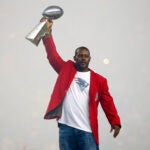 Former New England Patriots cornerback Ty Law raises one of the four Lombardi Trophies before an NFL football game between the New England Patriots and the Pittsburgh Steelers Thursday, Sept. 10, 2015, in Foxborough, Mass.