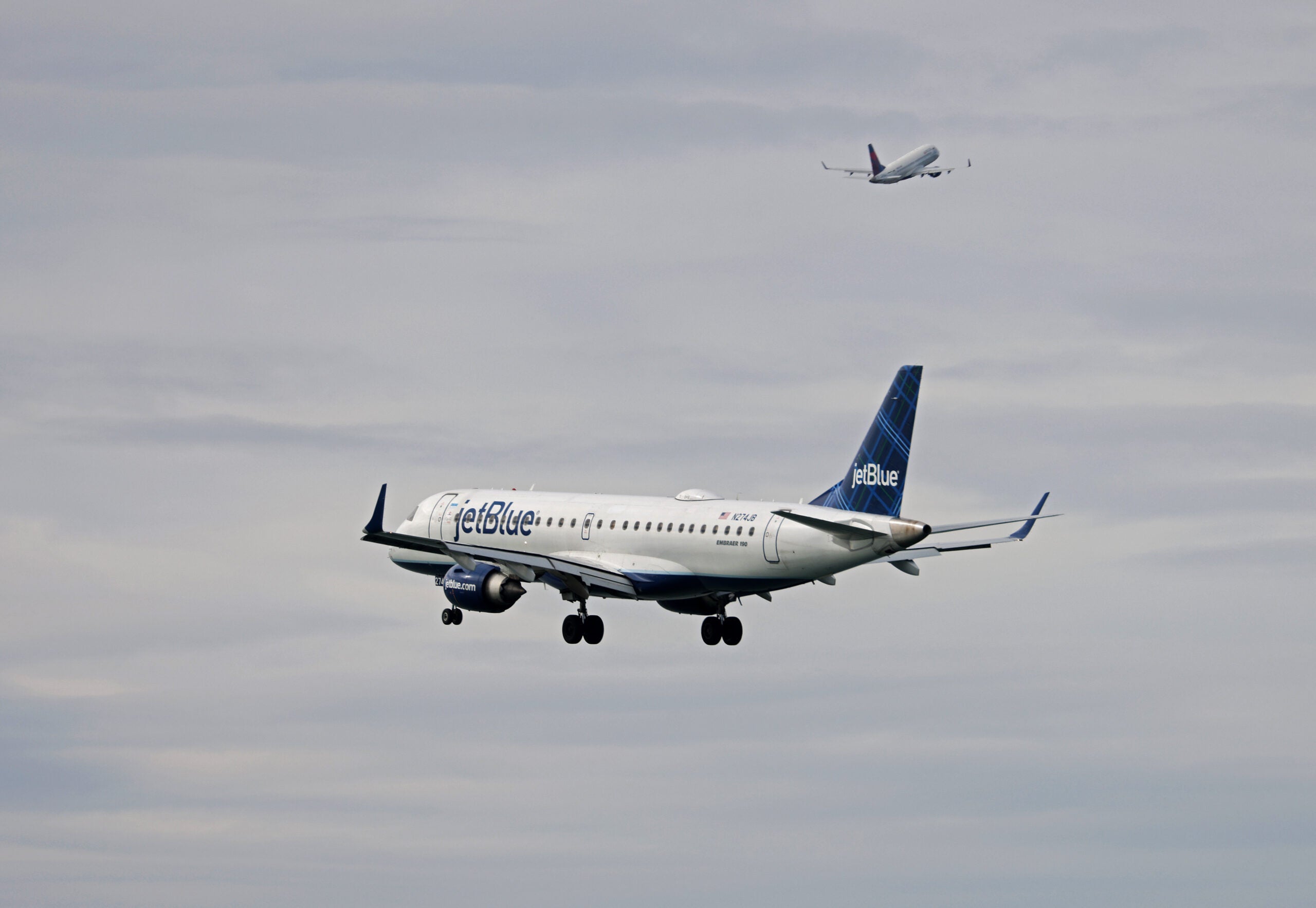 A JetBlue plane is seen flying in the sky, with another plane flying in the distance.