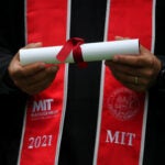 A graduate wearing Massachusetts Institute of Technology regalia and holding a diploma wrapped in a red bow.