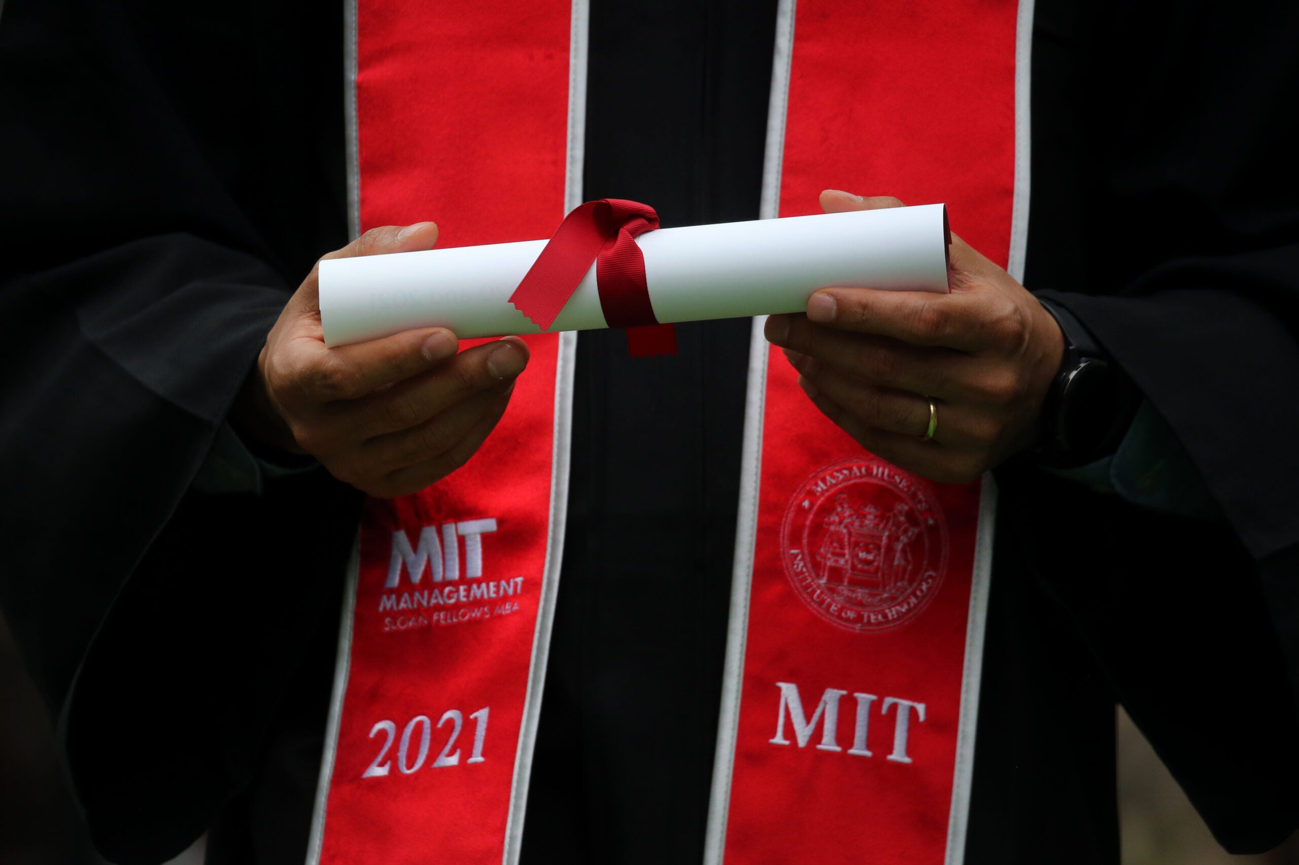 A graduate wearing Massachusetts Institute of Technology regalia and holding a diploma wrapped in a red bow.