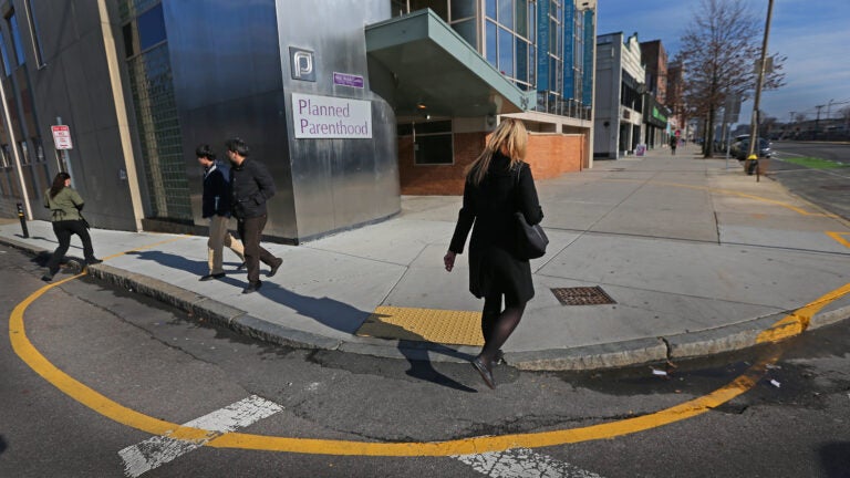 Four people are seen walking on a street, with a Planned Parenthood office in Boston in the background.