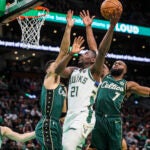 Jrue Holiday attacking the basket against multiple Celtics players.
