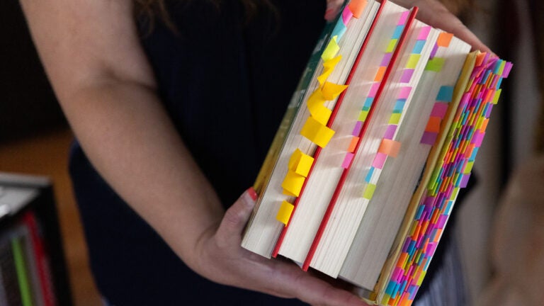 Jennifer Petersen holds a stack of books with sticky notes on various pages that she has read, flagged for sexual content, and challenged in Spotsylvania County Public Schools.