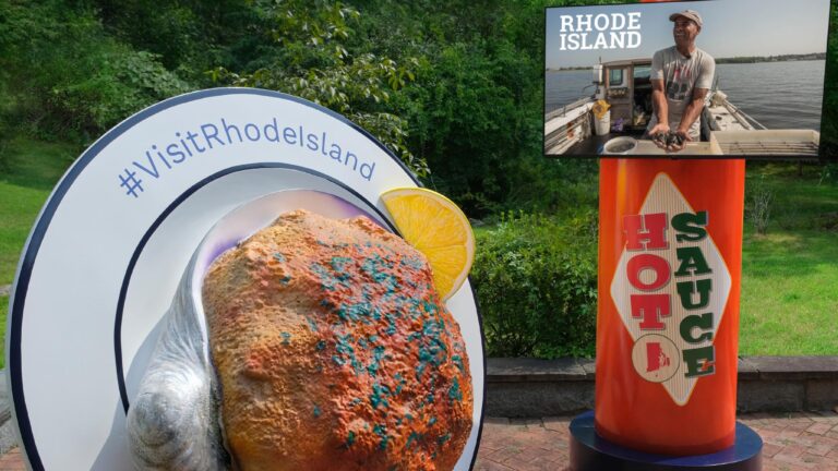 An image of a Rhode Island "stuffie" installation, a 200-pound styrofoam version of the baked clam, on a plate and next to an 8-foot bottle of hot sauce.