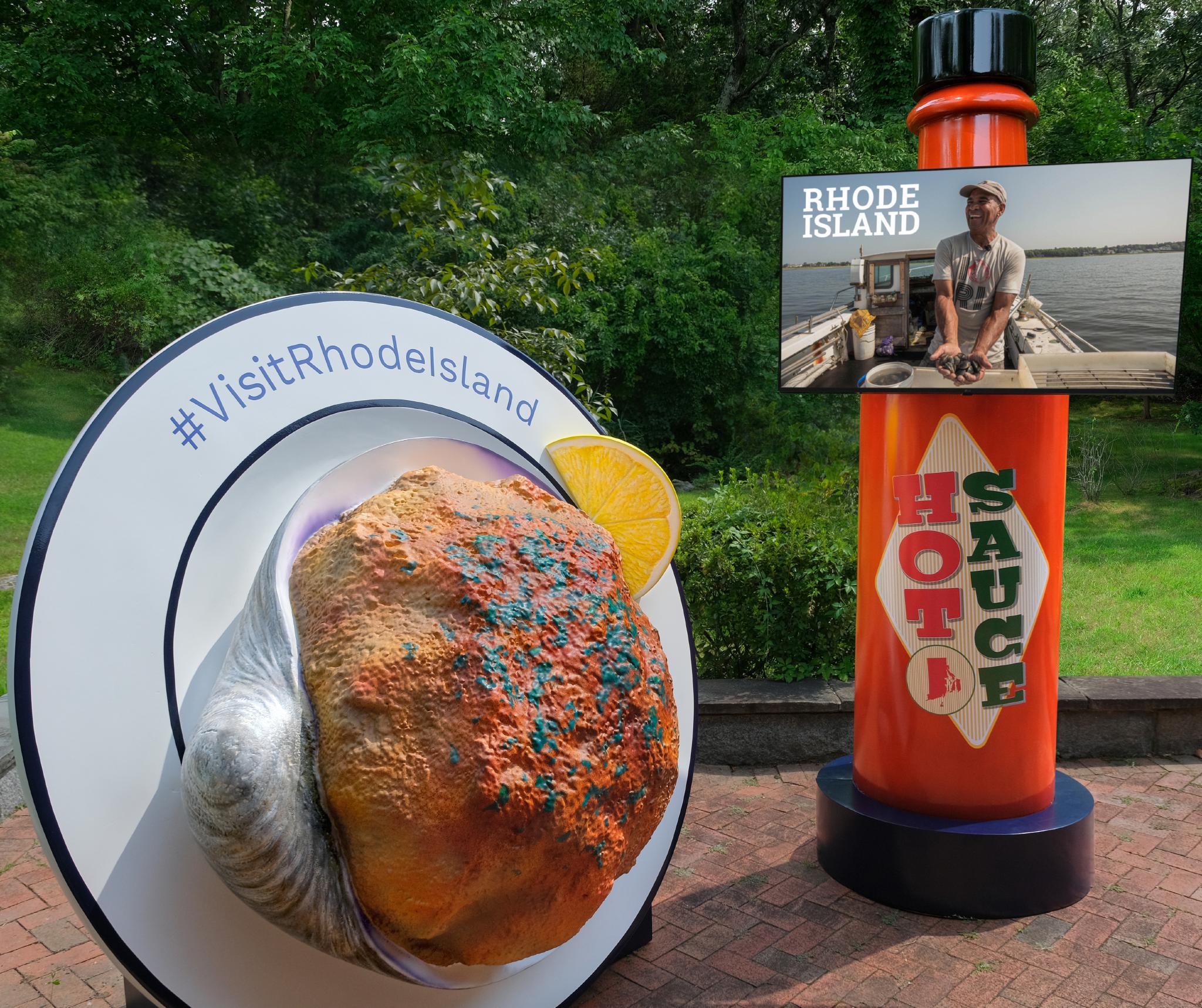 An image of a Rhode Island "stuffie" installation, a 200-pound styrofoam version of the baked clam, on a plate and next to an 8-foot bottle of hot sauce.