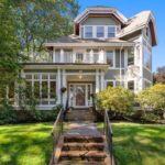 A single-family Victorian with tan siding and white trim with brick steps and an enclosed porch.