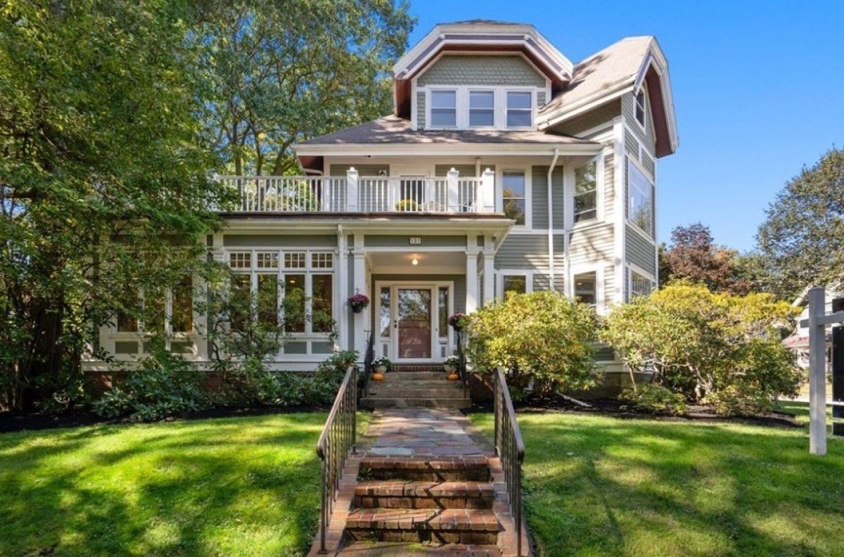 A single-family Victorian with tan siding and white trim with brick steps and an enclosed porch.