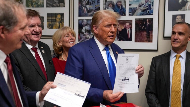 Republican presidential candidate former President Donald Trump talks as New Hampshire Secretary of State David Scanlan, left, listens as he signs papers.