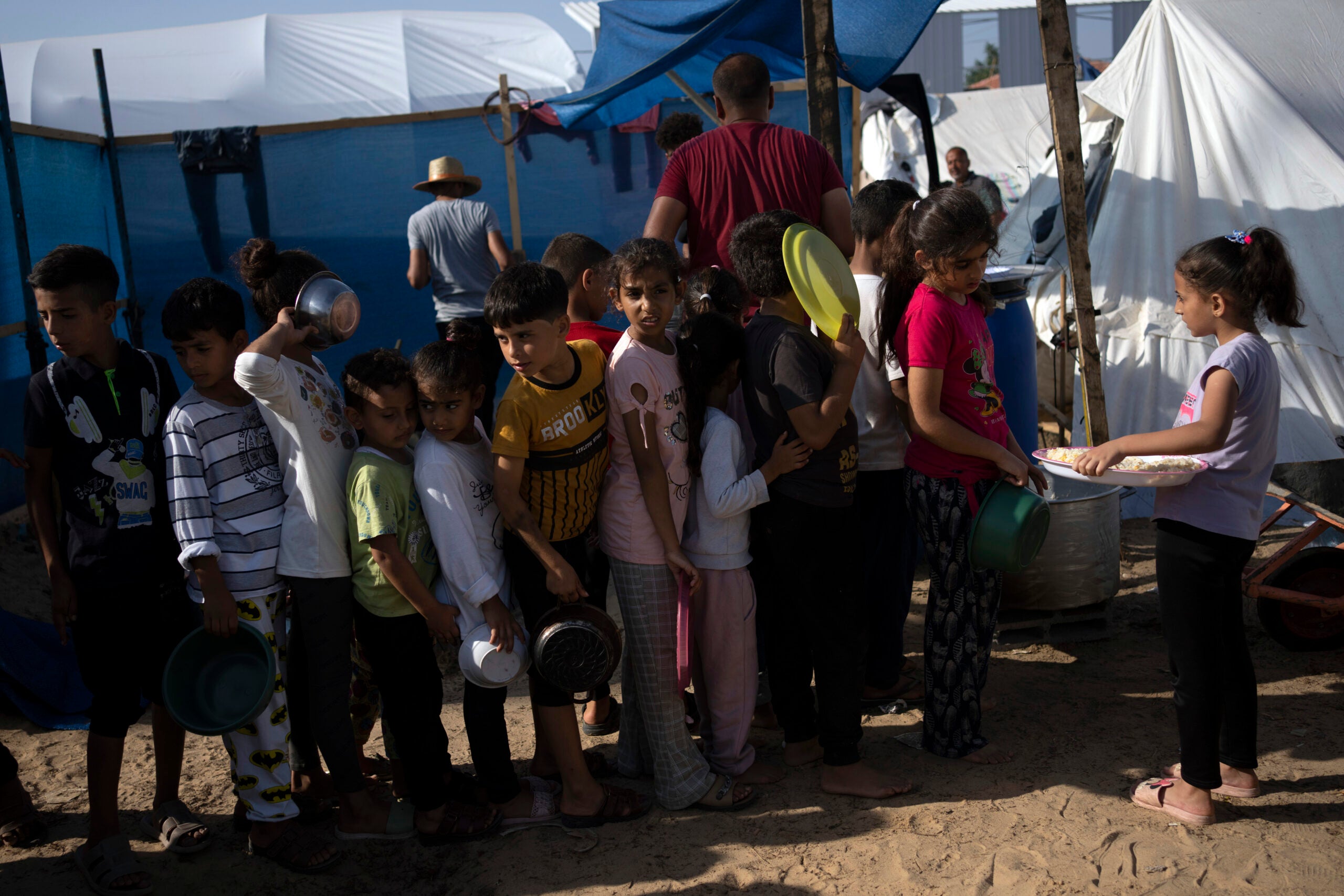 Palestinian children wait in line for a food distribution in a displaced tent camp, in Khan Younis.