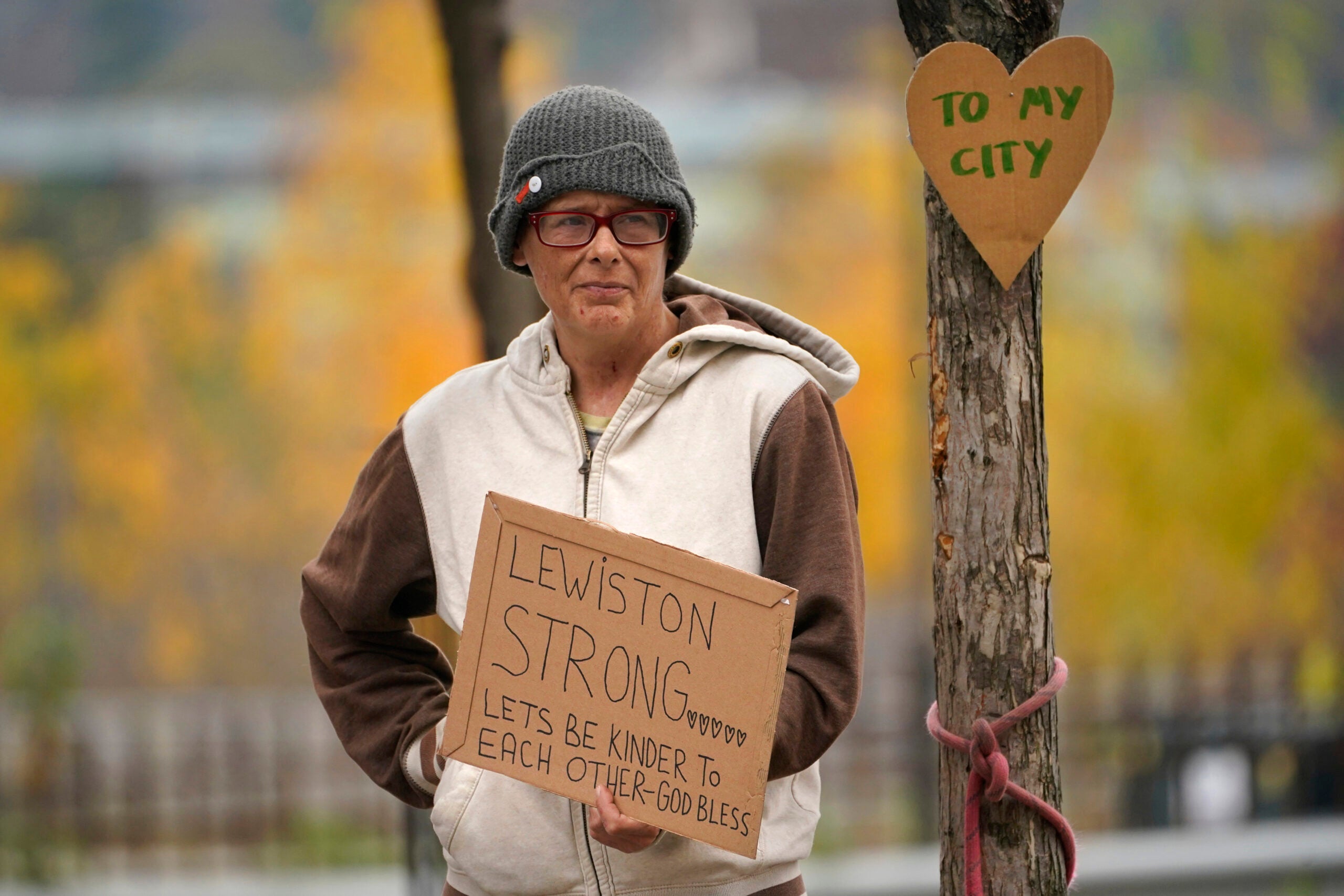 A woman stands outside with a sign in hand that reads "Lewiston strong" following a mass shooting.