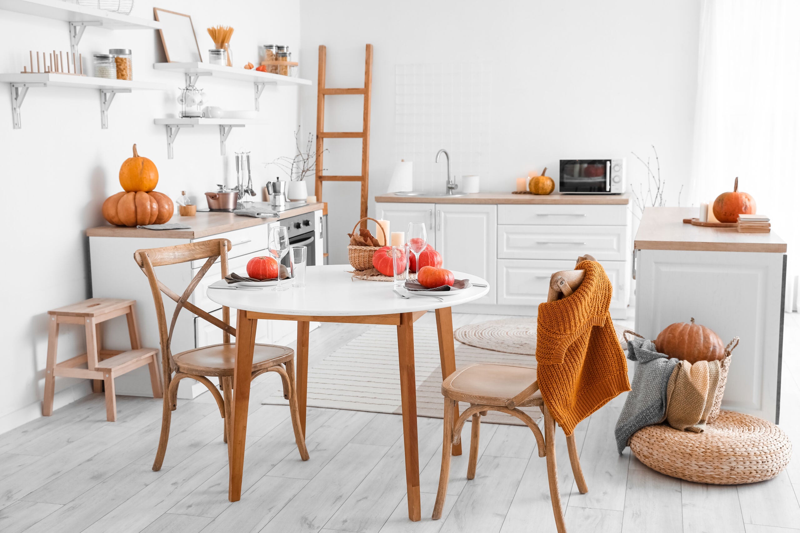 Interior of light kitchen with counters, dining table and pumpkins
