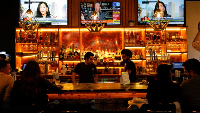 A lit-up bar holding multiple bottles of liquor, with two bartenders serving customers.