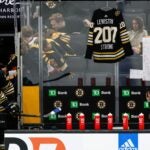 A hockey jersey hangs behind the Boston Bruins bench as a tribute to the victims of the mass shooting in Lewiston, Maine yesterday before a game between the Boston Bruins and the Anaheim Ducks at the TD Garden on October 26, 2023 in Boston, Massachusetts. The jersey says "Lewiston Strong 207" on the back.