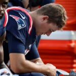 New England Patriots quarterback Mac Jones, right, is seated on bench near wide receiver DeVante Parker, left, during the first half of an NFL football game against the New Orleans Saints, Sunday, Oct. 8, 2023, in Foxborough, Mass.