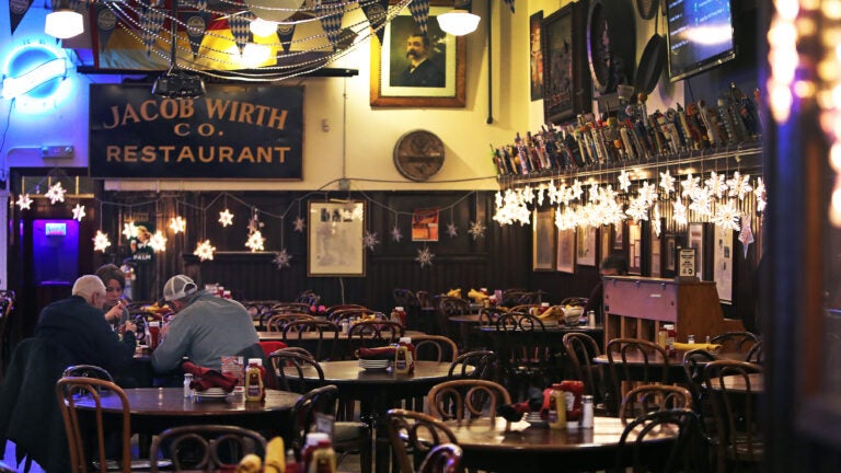 A couple of patrons sit at a wooden table among several empty chairs inside a restaurant and bar named Jacob Wirth in Boston.