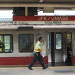 An MBTA inspector in a yellow vest walks by a Red Line train at the JFK/UMass station stop.