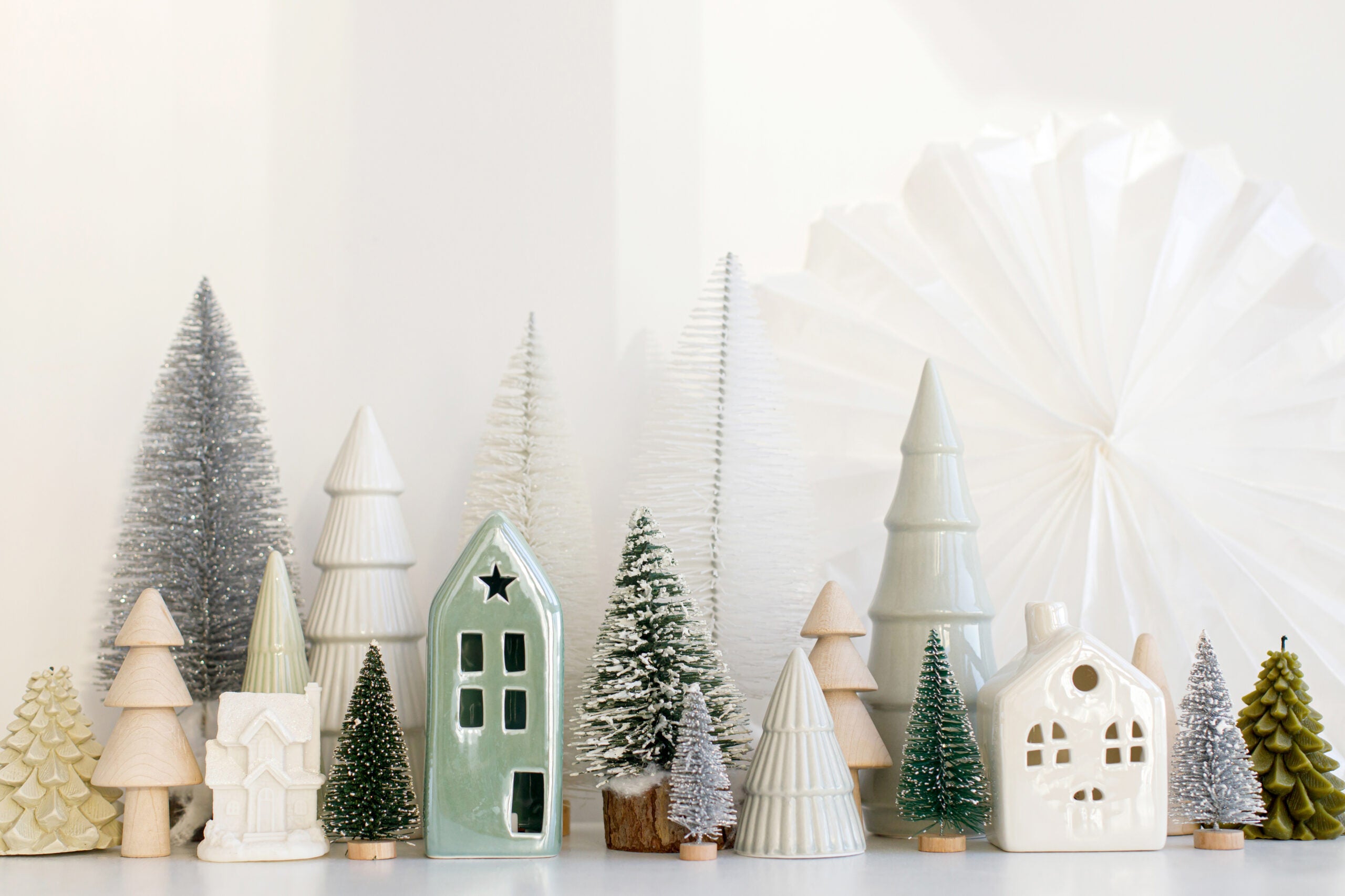 Modern christmas scene, miniature snowy village on white table. Merry Christmas! Stylish little Christmas trees and house decoration. Winter holiday banner, scandinavian monochromatic decor