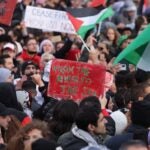 People, including one holding up a sign that reads: "From the River to the Sea", chant slogans under Palestinian flags during a "Freedom for Palestine" protest.