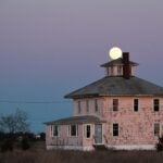 An image of a pink house with the moon in the background.