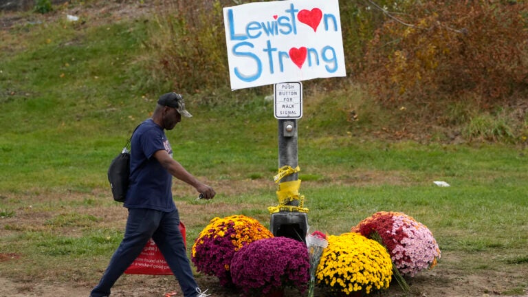 A man walks by flowers and a sign of support for the community in the wake of the mass shootings that occurred on Oct. 25, in Lewiston, Maine.