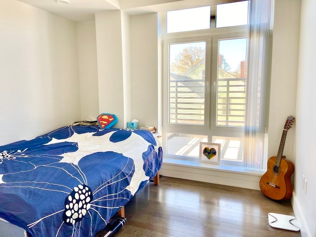 Bedroom with blue floral bedspread, wood floors, and a guitar. 